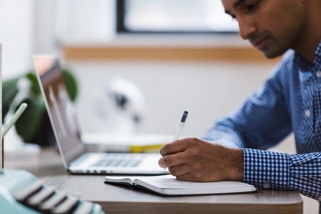 A man studying diligently with a laptop while writing notes